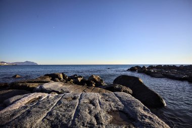 Küçük bir körfezden görünen ve dalgakıran kayaları tarafından çerçevelenen binalar ve uçurumun kenarındaki bir çıkıntının ucu.
