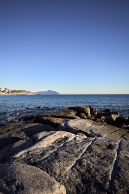 Küçük bir körfezden görünen ve dalgakıran kayaları tarafından çerçevelenen binalar ve uçurumun kenarındaki bir çıkıntının ucu.