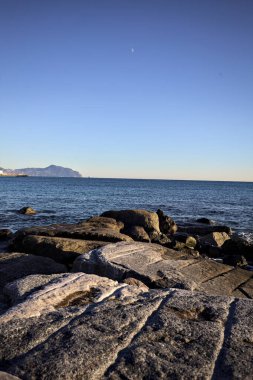 Küçük bir körfezden görünen ve dalgakıran kayaları tarafından çerçevelenen binalar ve uçurumun kenarındaki bir çıkıntının ucu.
