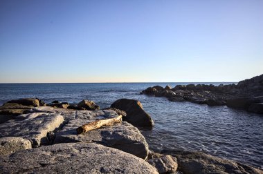Rocks of a cliff at sunset seen at water level with the sea stretching to the Horizon