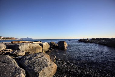 Küçük bir körfezden görünen ve dalgakıran kayaları tarafından çerçevelenen binalar ve uçurumun kenarındaki bir çıkıntının ucu.