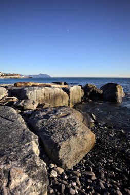 Küçük bir körfezden görünen ve dalgakıran kayaları tarafından çerçevelenen binalar ve uçurumun kenarındaki bir çıkıntının ucu.