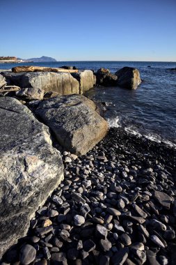 Küçük bir körfezden görünen ve dalgakıran kayaları tarafından çerçevelenen binalar ve uçurumun kenarındaki bir çıkıntının ucu.