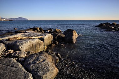 Küçük bir körfezden görünen ve dalgakıran kayaları tarafından çerçevelenen binalar ve uçurumun kenarındaki bir çıkıntının ucu.