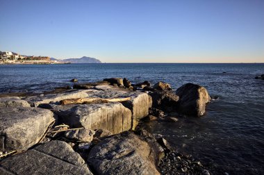 Küçük bir körfezden görünen ve dalgakıran kayaları tarafından çerçevelenen binalar ve uçurumun kenarındaki bir çıkıntının ucu.