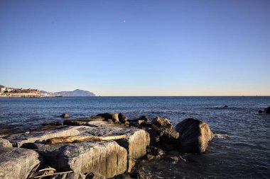 Küçük bir körfezden görünen ve dalgakıran kayaları tarafından çerçevelenen binalar ve uçurumun kenarındaki bir çıkıntının ucu.