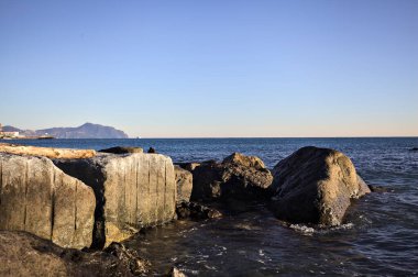 Küçük bir körfezden görünen ve dalgakıran kayaları tarafından çerçevelenen binalar ve uçurumun kenarındaki bir çıkıntının ucu.