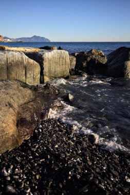 Küçük bir körfezden görünen ve dalgakıran kayaları tarafından çerçevelenen binalar ve uçurumun kenarındaki bir çıkıntının ucu.