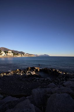 Deniz kenarındaki bina ve bulvar. Denizin üzerindeki küçük bir uçurumdan görülebiliyor. Kışın gün batımında sahneyi çerçeveliyorlar.