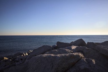 Gün batımında bir uçurumun kayaları su seviyesinde görülür ve deniz Horizon 'a kadar uzanır.