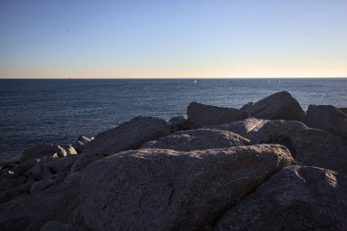 Gün batımında bir uçurumun kayaları su seviyesinde görülür ve deniz Horizon 'a kadar uzanır.