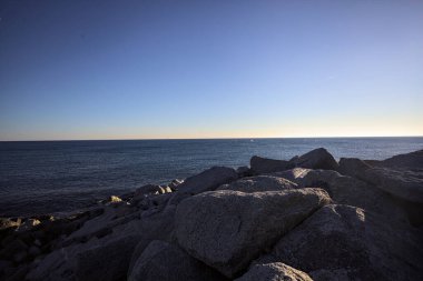 Rocks of a cliff at sunset seen at water level with the sea stretching to the Horizon