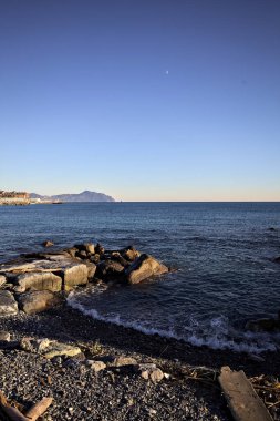 Küçük bir körfezden görünen ve dalgakıran kayaları tarafından çerçevelenen binalar ve uçurumun kenarındaki bir çıkıntının ucu.