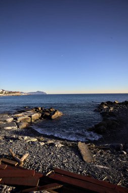 Küçük bir körfezden görünen ve dalgakıran kayaları tarafından çerçevelenen binalar ve uçurumun kenarındaki bir çıkıntının ucu.