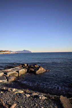 Küçük bir körfezden görünen ve dalgakıran kayaları tarafından çerçevelenen binalar ve uçurumun kenarındaki bir çıkıntının ucu.