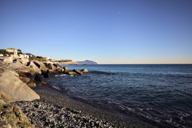 Küçük bir körfezden görünen ve dalgakıran kayaları tarafından çerçevelenen binalar ve uçurumun kenarındaki bir çıkıntının ucu.