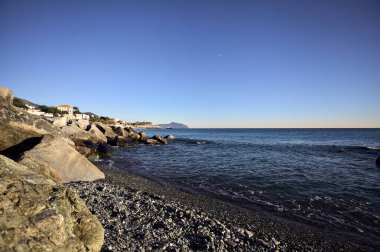 Küçük bir körfezden görünen ve dalgakıran kayaları tarafından çerçevelenen binalar ve uçurumun kenarındaki bir çıkıntının ucu.
