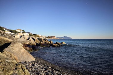 Küçük bir körfezden görünen ve dalgakıran kayaları tarafından çerçevelenen binalar ve uçurumun kenarındaki bir çıkıntının ucu.