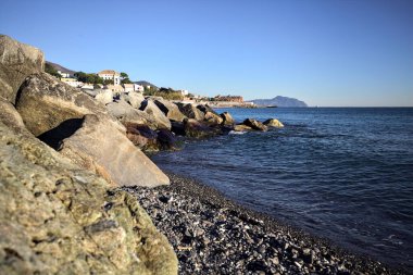 Küçük bir körfezden görünen ve dalgakıran kayaları tarafından çerçevelenen binalar ve uçurumun kenarındaki bir çıkıntının ucu.