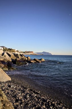 Küçük bir körfezden görünen ve dalgakıran kayaları tarafından çerçevelenen binalar ve uçurumun kenarındaki bir çıkıntının ucu.