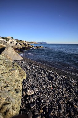 Küçük bir körfezden görünen ve dalgakıran kayaları tarafından çerçevelenen binalar ve uçurumun kenarındaki bir çıkıntının ucu.