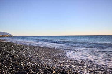 Gün batımında ufukta deniz uzanan bir çakıl taşı plajının ön kıyısı.