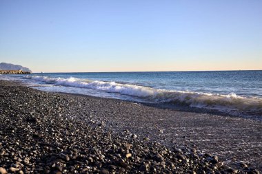 Gün batımında ufukta deniz uzanan bir çakıl taşı plajının ön kıyısı.