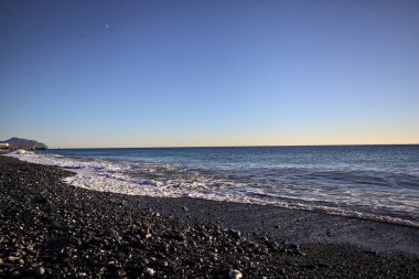 Gün batımında ufukta deniz uzanan bir çakıl taşı plajının ön kıyısı.