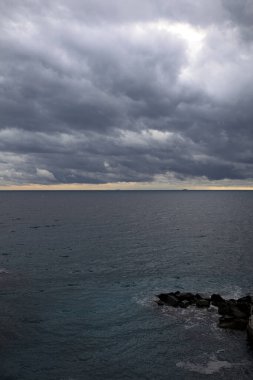 Alacakaranlıkta bulutlu bir günde ufka doğru uzanan deniz yukarıdan görünen küçük bir koydan kayalarla birlikte.