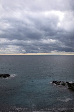 Alacakaranlıkta bulutlu bir günde ufka doğru uzanan deniz yukarıdan görünen küçük bir koydan kayalarla birlikte.