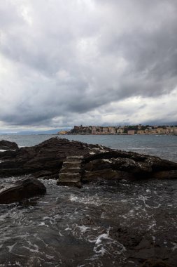 Alacakaranlıkta bulutlu bir günde, deniz kenarındaki bir körfezdeki kayanın yanındaki küçük merdivende.