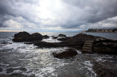 Alacakaranlıkta bulutlu bir günde, deniz kenarındaki bir körfezdeki kayanın yanındaki küçük merdivende.