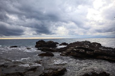 Alacakaranlıkta bulutlu bir günde, deniz kenarındaki bir körfezdeki kayanın yanındaki küçük merdivende.