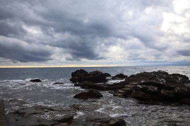 Alacakaranlıkta bulutlu bir günde, deniz kenarındaki bir körfezdeki kayanın yanındaki küçük merdivende.