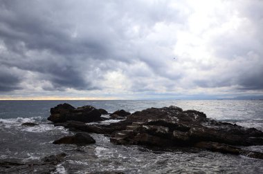 Alacakaranlıkta bulutlu bir günde, deniz kenarındaki bir körfezdeki kayanın yanındaki küçük merdivende.