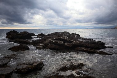 Alacakaranlıkta bulutlu bir günde, deniz kenarındaki bir körfezdeki kayanın yanındaki küçük merdivende.
