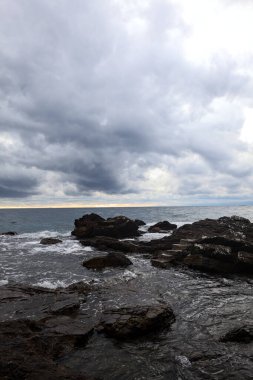 Alacakaranlıkta bulutlu bir günde, deniz kenarındaki bir körfezdeki kayanın yanındaki küçük merdivende.