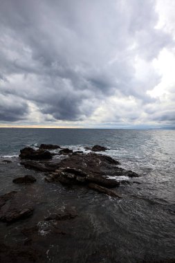 Alacakaranlıkta bulutlu bir günde, deniz kenarındaki bir körfezdeki kayanın yanındaki küçük merdivende.