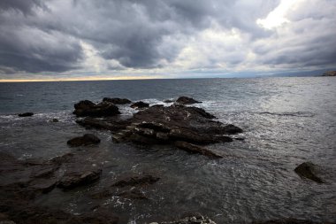 Alacakaranlıkta bulutlu bir günde, deniz kenarındaki bir körfezdeki kayanın yanındaki küçük merdivende.