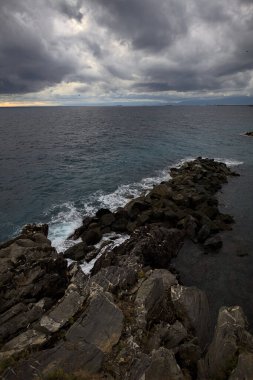 Alacakaranlıkta bulutlu bir günde, bir uçurumun kayaları ve dalgaların altında ezildiği dalgalar.