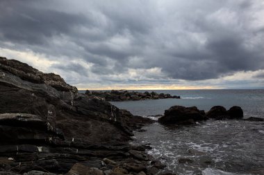 Alacakaranlıkta bulutlu bir günde, bir uçurumun kayaları ve dalgaların altında ezildiği dalgalar.