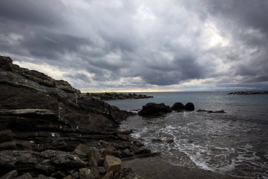 Alacakaranlıkta bulutlu bir günde, bir uçurumun kayaları ve dalgaların altında ezildiği dalgalar.