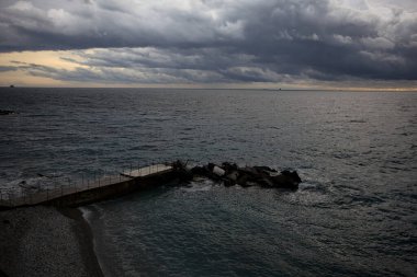 Dalgalar, alacakaranlıkta bulutlu bir günde, küçük bir koydan engebeli bir denize doğru uzanır. Üzerlerindeki kayalıklardan görülür. Arka planda fildişi uçları vardır.