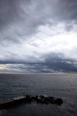 Dalgalar, alacakaranlıkta bulutlu bir günde, küçük bir koydan engebeli bir denize doğru uzanır. Üzerlerindeki kayalıklardan görülür. Arka planda fildişi uçları vardır.