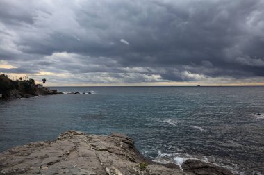Denizin üzerindeki uçurum ufka doğru uzanıyor. Alacakaranlıkta bulutlu bir günde kayalara çarpan suyla birlikte.