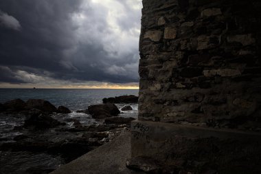 Deniz kıyısındaki bir viyadük kemerleri, bir dalgakıranın kayaları üzerinde, alacakaranlıkta bulutlu bir günde görülür.