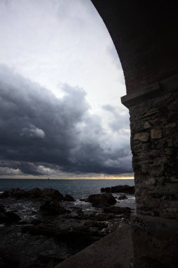 Deniz kıyısındaki bir viyadük kemerleri, bir dalgakıranın kayaları üzerinde, alacakaranlıkta bulutlu bir günde görülür.