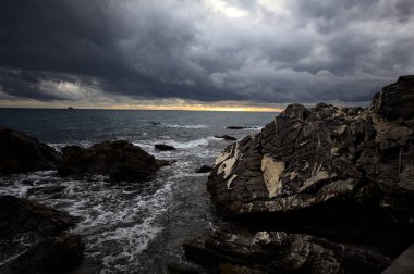 Alacakaranlıkta bulutlu bir günde kayalara vuran suyla dalgalı su