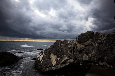 Alacakaranlıkta bulutlu bir günde kayalara vuran suyla dalgalı su