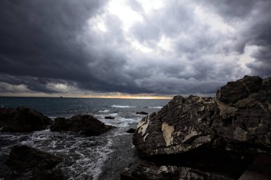 Alacakaranlıkta bulutlu bir günde kayalara vuran suyla dalgalı su